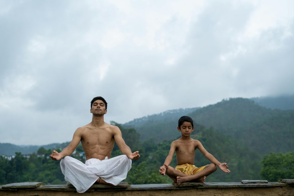 A father and son meditating outdoors in serene mountain landscape. Promotes mindfulness and family bonding.