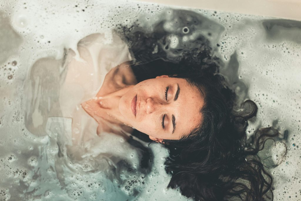 Woman with long hair enjoying a peaceful bubble bath with eyes closed, illustrating relaxation.