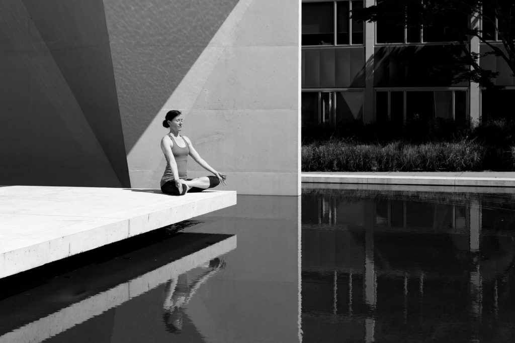 A woman meditating by a poolside, reflecting tranquility and focus in a minimalist setting.