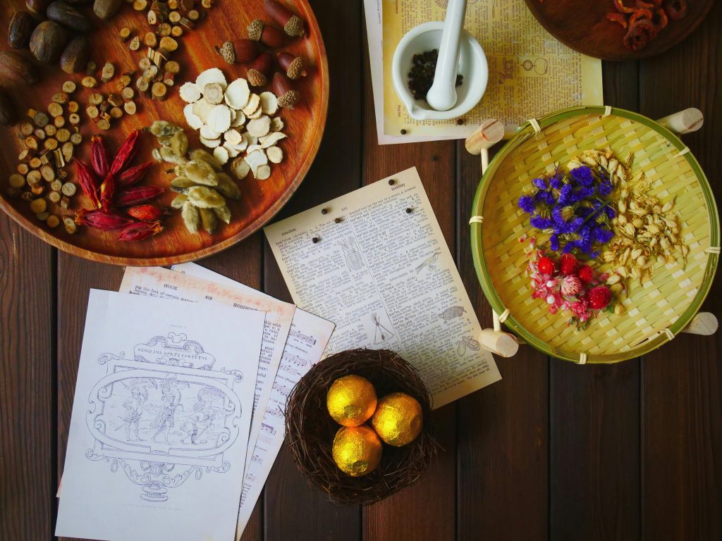 Overhead view of traditional herbs and ingredients for medicine making, featuring a ceramic mortar and vibrant dried flowers.