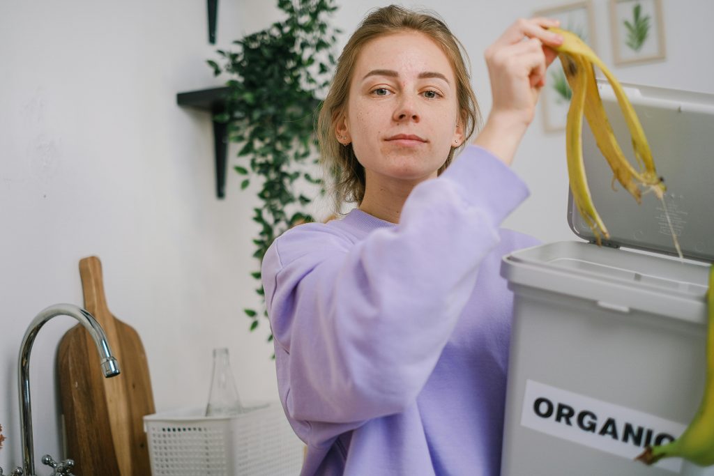 Woman disposing banana peel in organic bin at home kitchen, promoting eco-friendly lifestyle.