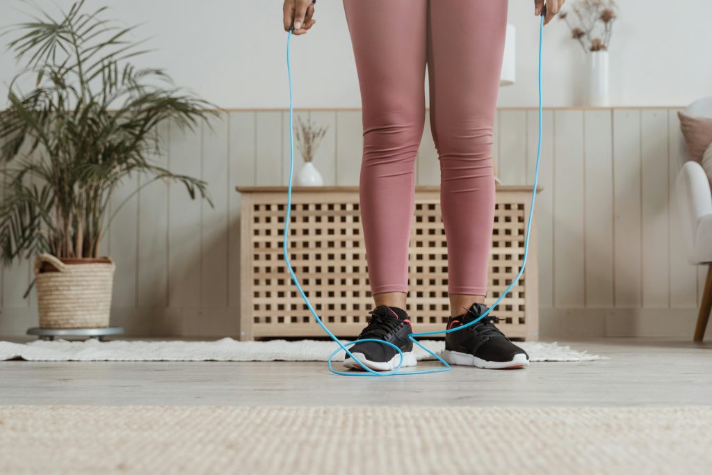 Woman in pink activewear exercising indoors with a jump rope.